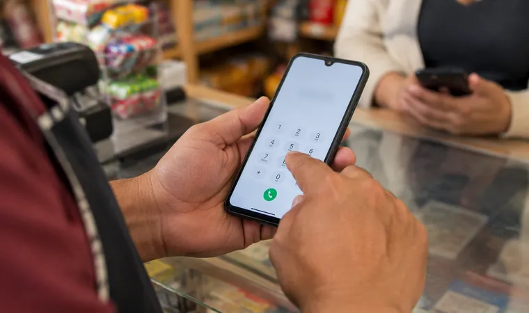 Tendero escribiendo el número del cliente en el celular para enviar una recarga
